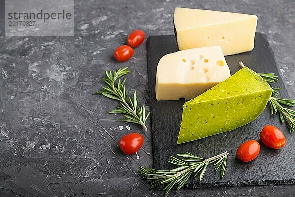 Grüner Basilikumkäse und verschiedene Käsesorten mit Rosmarin und Tomaten auf einer schwarzen Schiefertafel auf einem schwarzen Betonhintergrund. Seitenansicht  Nahaufnahme  Kopierraum  selektiver Fokus