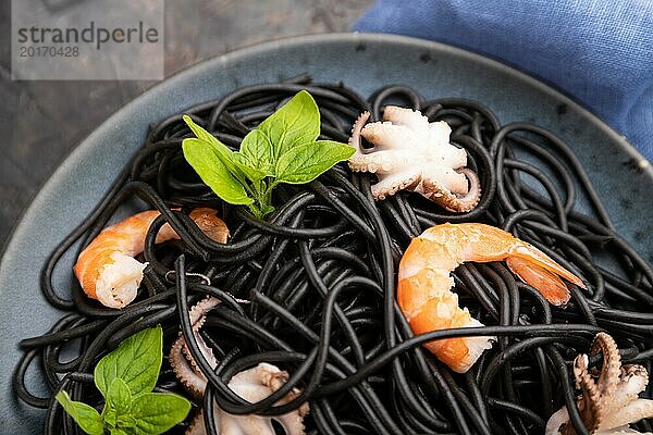 Schwarze Tintenfischnudeln mit Garnelen und kleinen Tintenfischen auf schwarzem Betonhintergrund und blauem Textil. Draufsicht  Nahaufnahme  selektiver Fokus