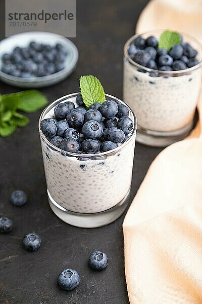 Joghurt mit Heidelbeeren und Chia im Glas auf schwarzem Betonhintergrund und orangefarbenem Leinenstoff. Seitenansicht  Nahaufnahme