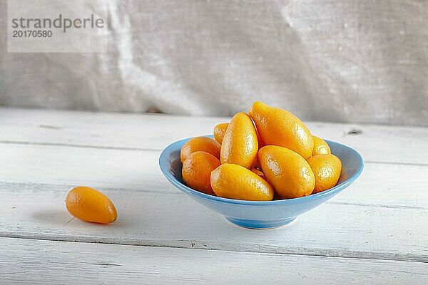 Kumquats in einem blauen Teller auf weißem Holzuntergrund  Nahaufnahme