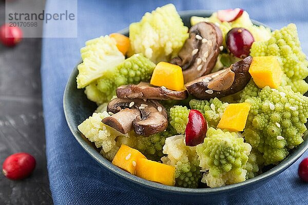 Vegetarischer Salat aus Romanesco Kohl  Champignons  Preiselbeeren  Avocado und Kürbis auf schwarzem Betonhintergrund und blauem Textil. Seitenansicht  Nahaufnahme  selektiver Fokus