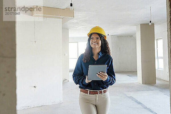 Lächelnder junger Architekt hält Tablet-PC in der Hand und untersucht vor Ort