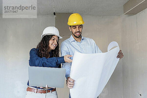 Glückliche Architekten diskutieren mit Bauplan und Laptop vor Ort