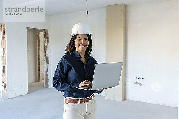 Lächelnder Architekt mit Schutzhelm und Laptop vor Ort