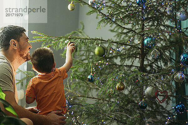 Junge schmückt mit Vater zu Hause den Weihnachtsbaum