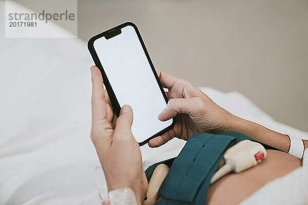 Hände einer schwangeren Frau  die ihr Mobiltelefon benutzt