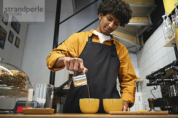 Junger Barista gießt Kaffee in Tasse im Café