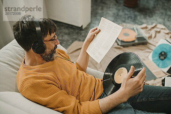 Mann hört Musik und liest Zeitung und hält zu Hause Schallplatte