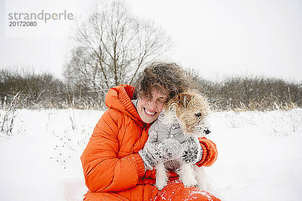 Glückliche Frau umarmt Hund auf Schneefeld