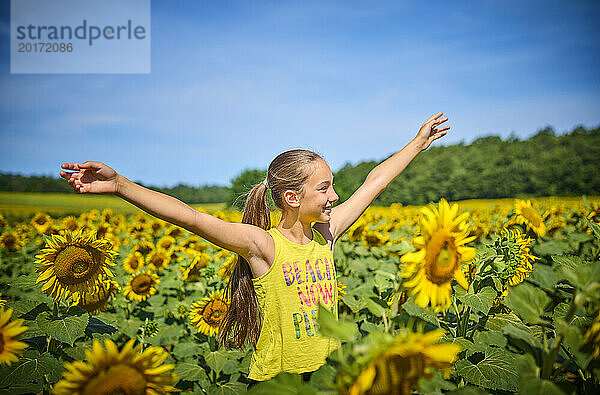 Glückliches Mädchen mit ausgestreckten Armen im Sonnenblumenfeld