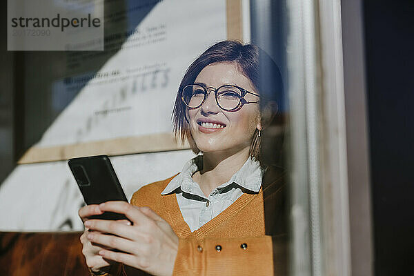 Glückliche Frau benutzt Smartphone  gesehen durch Glas