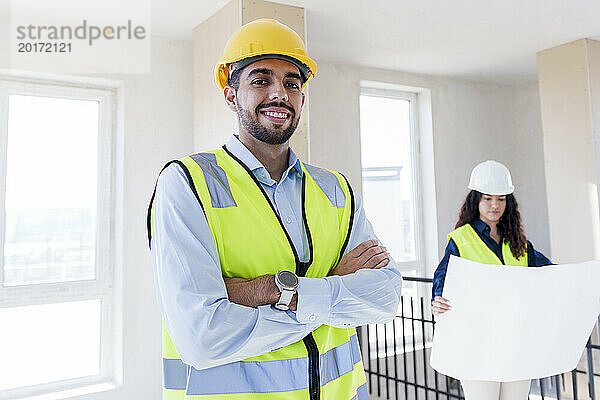 Smiling confident architect with colleague in background at site
