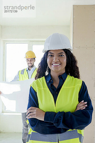 Smiling young architect standing with arms crossed at site