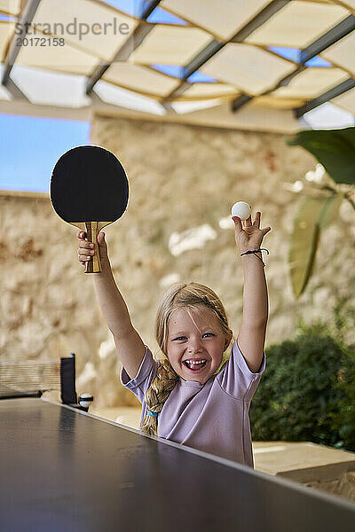 Fröhliches Mädchen jubelt mit Tischtennisschläger und Ball in der Villa