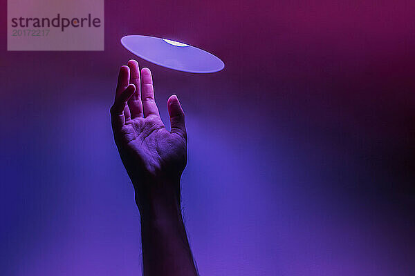 Hand eines Mannes unter Neonbeleuchtung vor farbigem Hintergrund