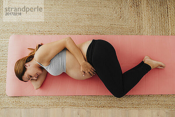 Schwangere Frau liegt zu Hause auf einer Trainingsmatte