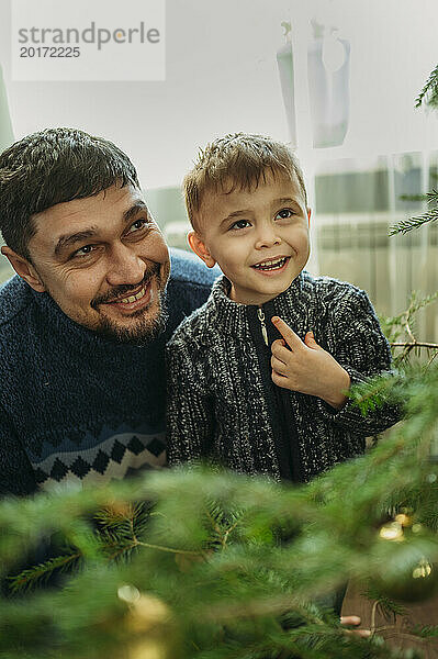 Lächelnder Mann schaut mit seinem Sohn zu Hause auf den Weihnachtsbaum