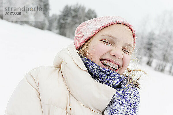 Fröhliches Mädchen mit geschlossenen Augen in warmer Kleidung auf dem Schneefeld