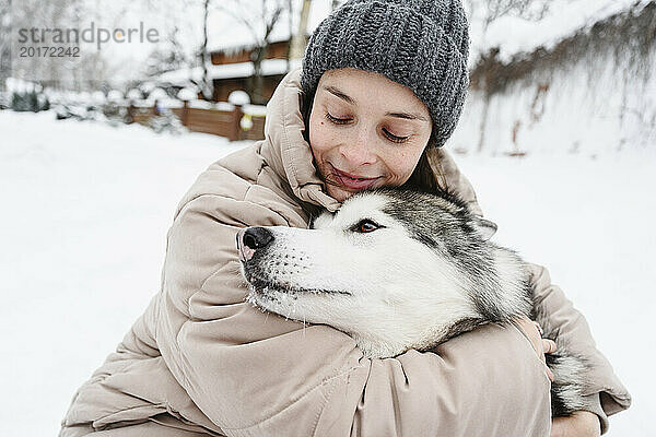Lächelnde Frau umarmt Husky-Hund im Schnee