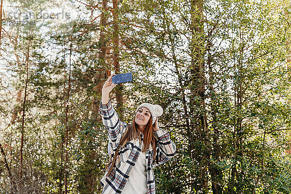 Glückliche Frau macht ein Selfie mit ihrem Smartphone und steht vor einem Baum