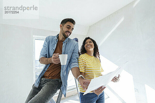 Lächelndes Paar diskutiert über den Bauplan für die Renovierung seines neuen Zuhauses