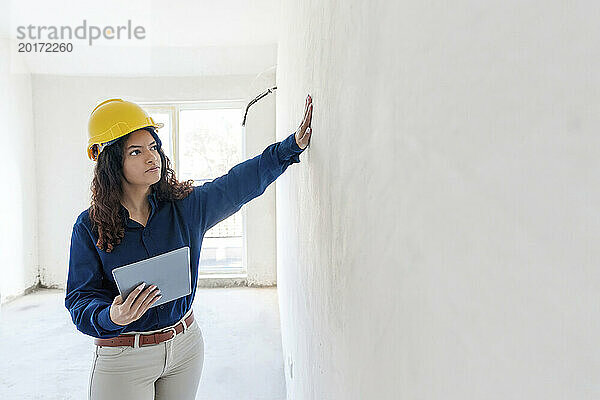 Architekt hält Tablet-PC in der Hand und untersucht Wand auf Baustelle