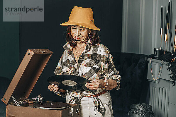 Lächelnde Frau hält Schallplatte neben Plattenspieler zu Hause