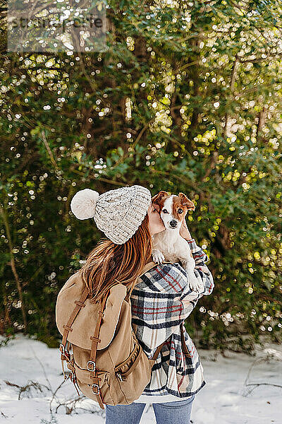 Frau mit Strickmütze und küssendem Hund im Winter