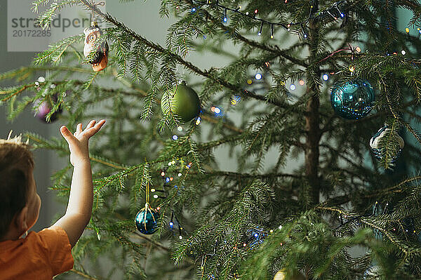 Junge hängt Weihnachtsschmuck an Baum zu Hause