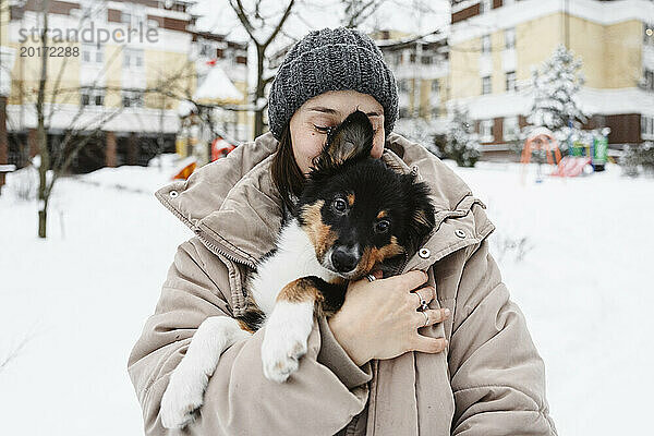 Frau bedeckt Hund mit Winterjacke im Schnee