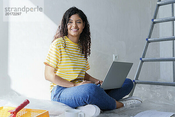 Lächelnde Frau sitzt mit Laptop im neuen Zuhause