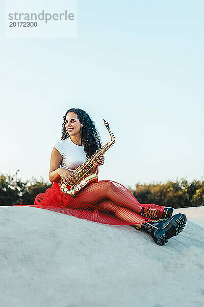 Lächelnde Frau mit Saxophon sitzt im Skatepark