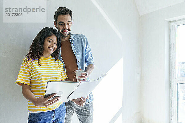 Glückliches Paar mit Tablet-PC analysiert Bauplan für Renovierung im neuen Zuhause