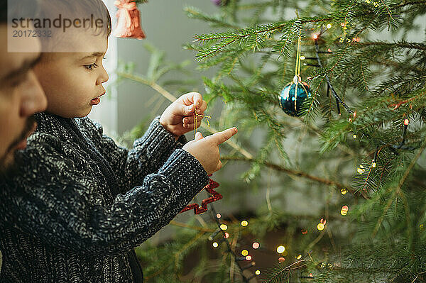 Kleiner Junge schmückt zu Hause den Weihnachtsbaum