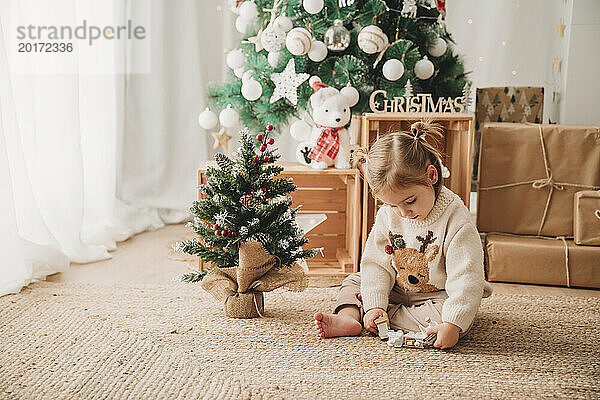 Mädchen spielt zu Hause mit Weihnachtsdekoration am Baum