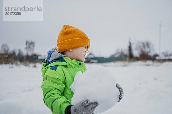 Lächelnder Junge hält Schneeball im Winter