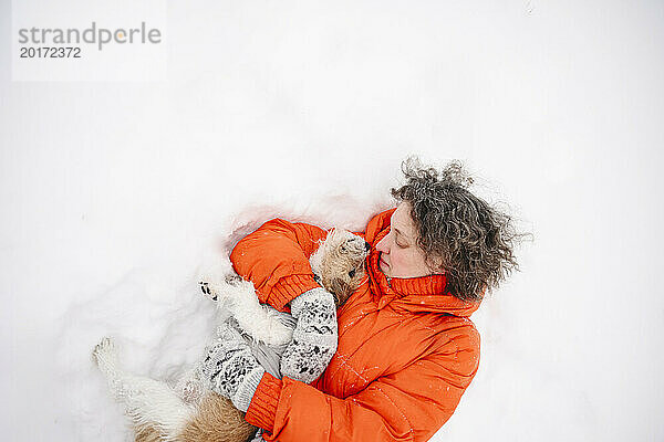 Frau liegt mit Hund im Schnee
