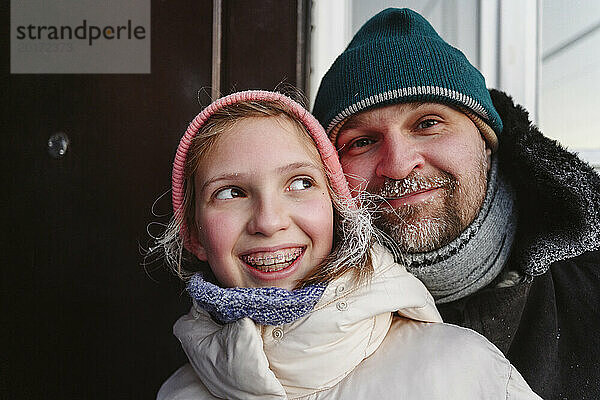 Lächelndes Mädchen mit Vater in warmer Kleidung zu Hause