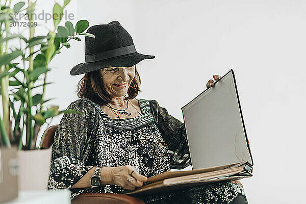 Lächelnde Seniorin schaut sich Fotoalbum vor weißem Hintergrund an