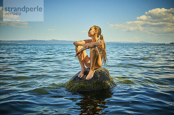 Mädchen sitzt auf einem Felsen im Bolsenasee  Italien