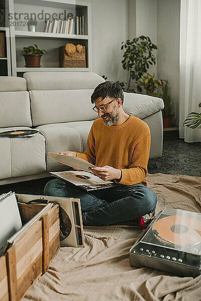 Lächelnder Mann sitzt mit Schallplatten zu Hause