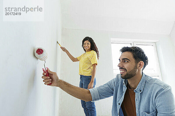 Happy couple applying paint on wall at new home