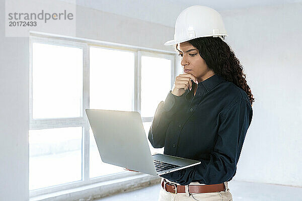 Architekt mit Schutzhelm und Laptop vor Ort