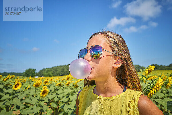 Mädchen bläst Kaugummi im Sonnenblumenfeld an einem sonnigen Tag