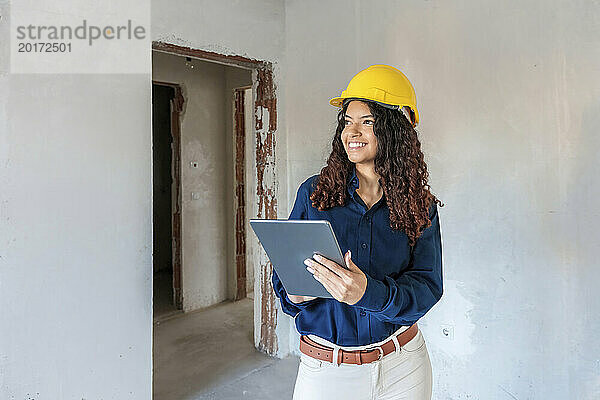 Lächelnder junger Architekt untersucht die Baustelle und hält einen Tablet-PC in der Hand