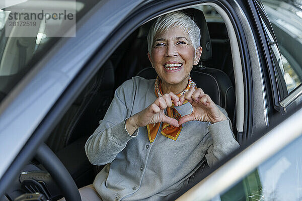Glückliche Frau gestikuliert Herzform im Auto im Ausstellungsraum