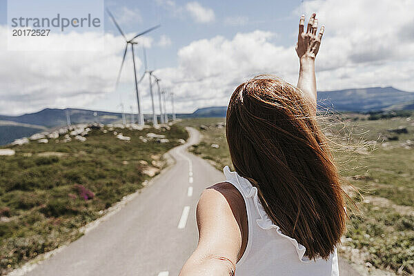 Spain  Madrid  Back of woman reaching toward clouds in front of wind farm