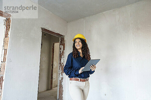 Lächelnder Architekt mit gelbem Helm und Tablet-PC vor Ort