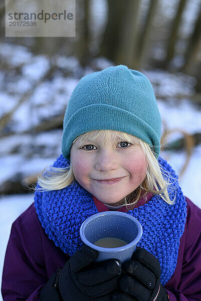 Smiling girl wearing warm clothes and holding mug in winter