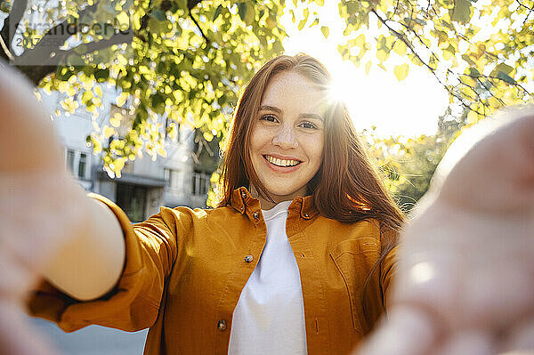 Glückliche Frau  die an einem sonnigen Tag ein Selfie in der Nähe eines Baumes macht